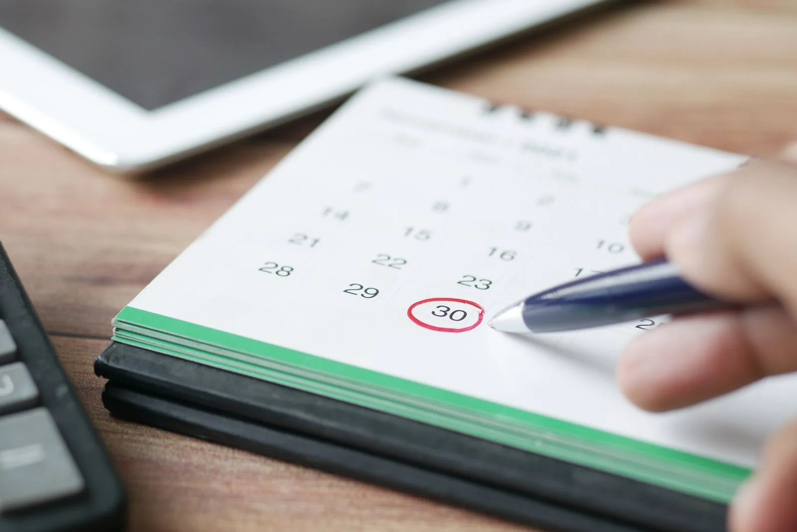 Mão circula com caneta vermelha o dia 30 em um calendário de mesa, ao lado de uma calculadora